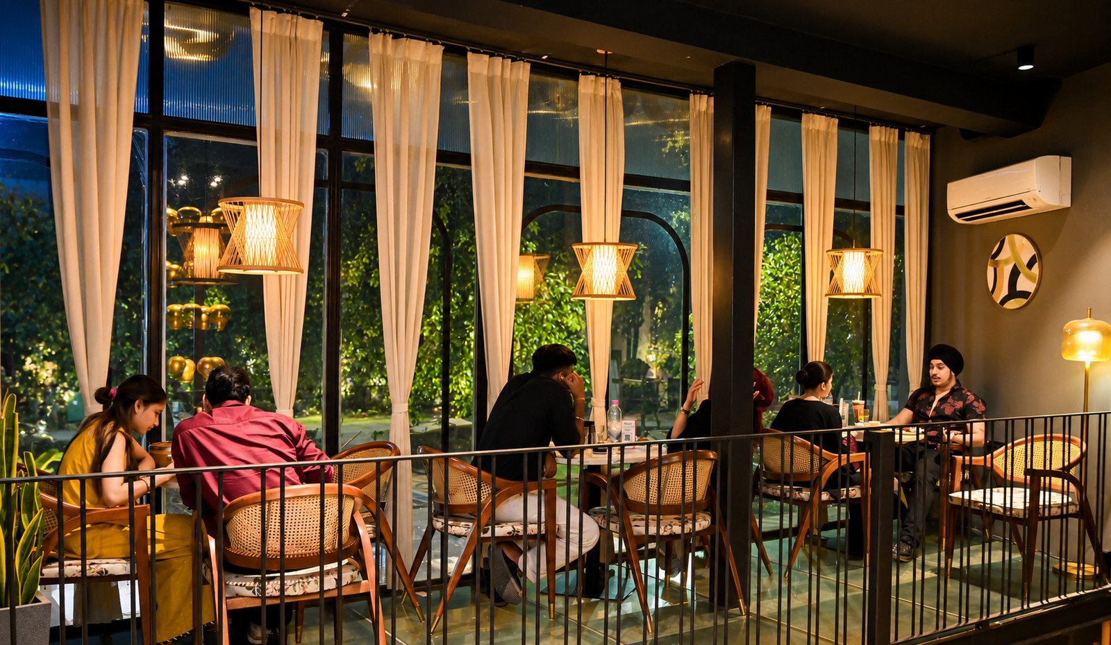 Guests at dinner on the first floor, under woven lamps beside tall curtained windows